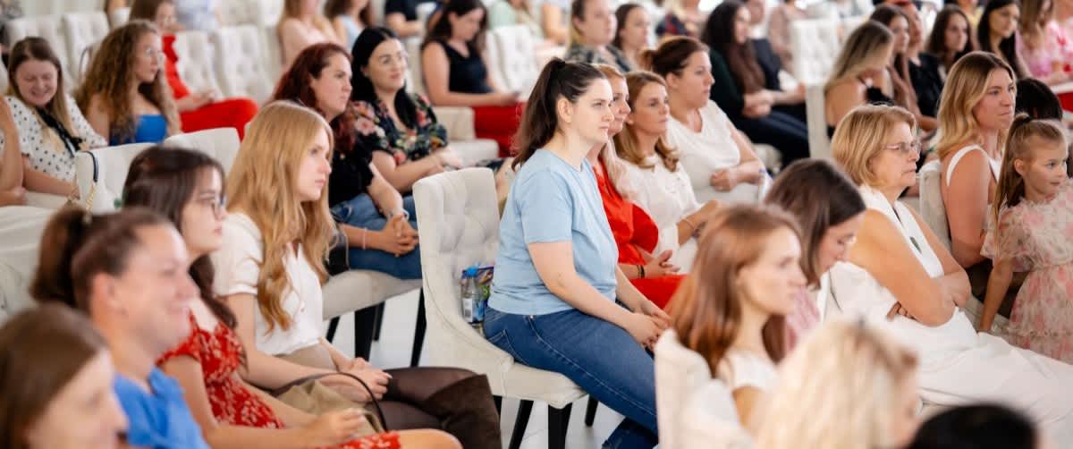 Audiență formată din femei care urmăresc o prezentare într-o sală de conferințe