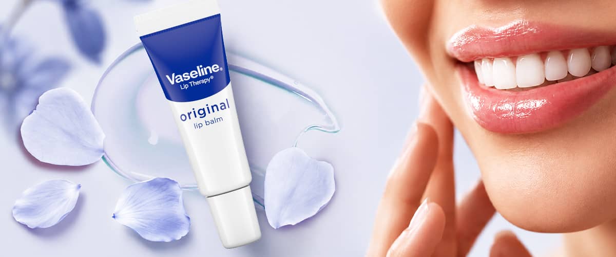 Balsam de buze Vaseline original lângă petale albastre și zâmbet cu buze hidratate