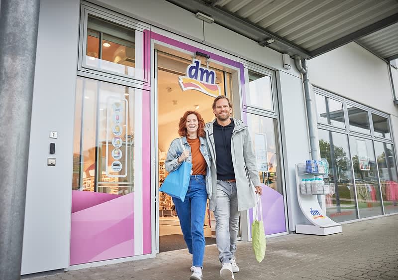 Cuplu zâmbitor ieșind dintr-un magazin dm ținând sacoșe de cumpărături