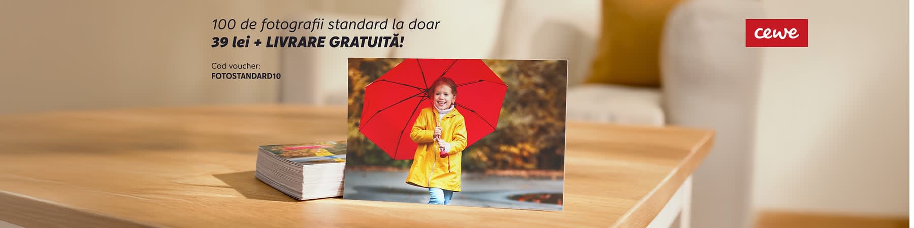 Cartonaș foto dreptunghiular sprijinit pe o masă de lemn, cu o parte dintr-o umbrelă roșie vizibilă pe fața cartonașului și colțul dreapta-sus etichetat cu logo-ul roșu „cew”