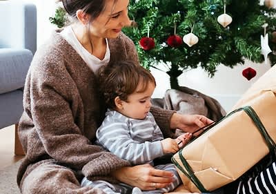 Mutter spielt mit Baby vor Weihnachtsbaum