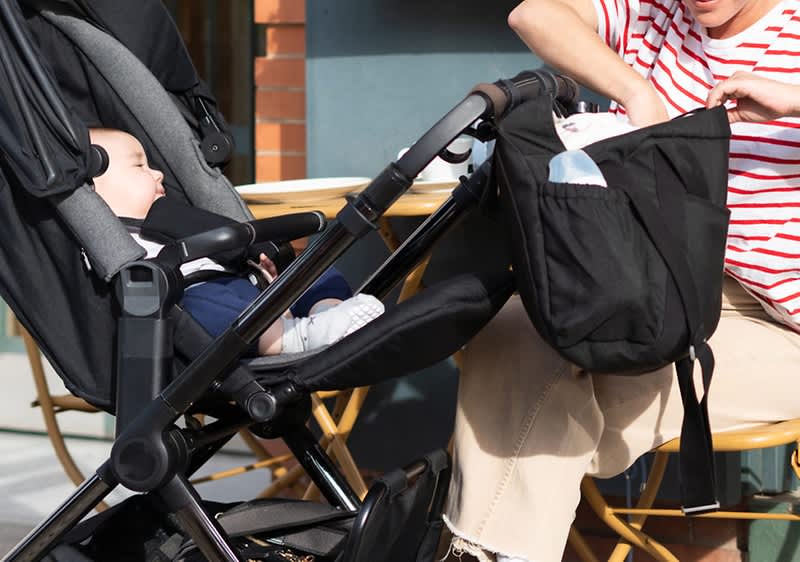 Frau kramt in windeltasche, die am Kinderwagen hängt