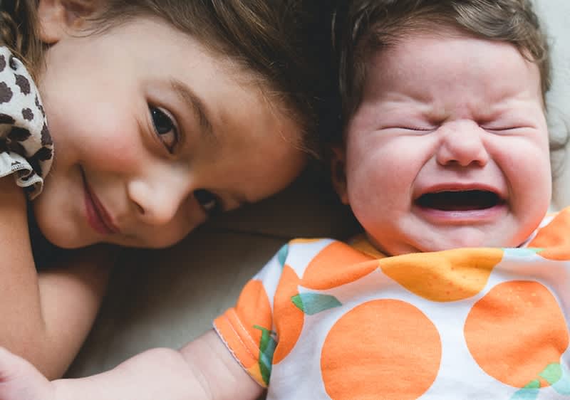 Lächelndes Mädchen liegt neben weinendem Baby