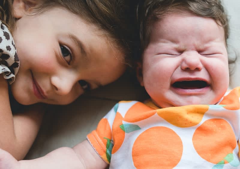 Lächelndes Mädchen liegt neben weinendem Baby
