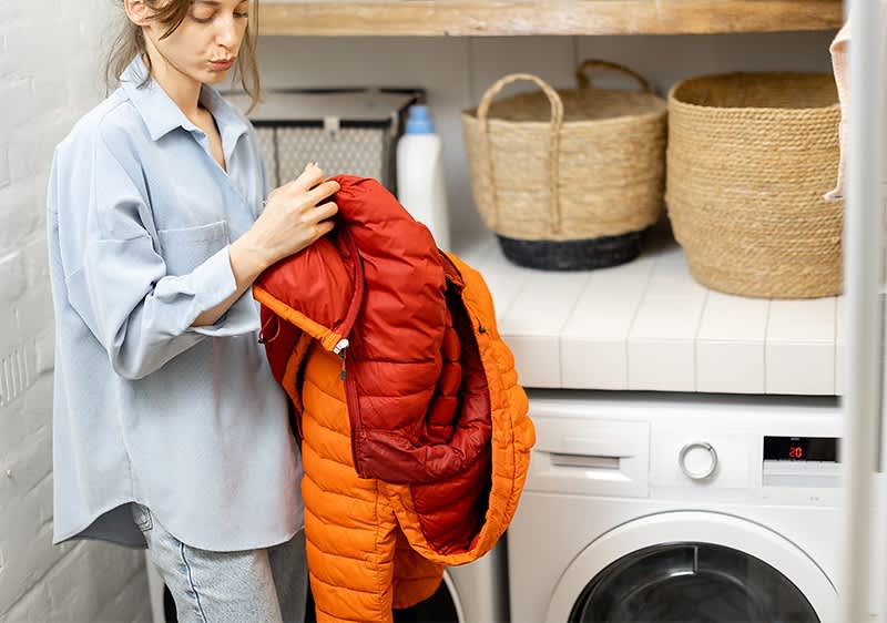 Frau mit Daunenjacke vor Waschmaschine