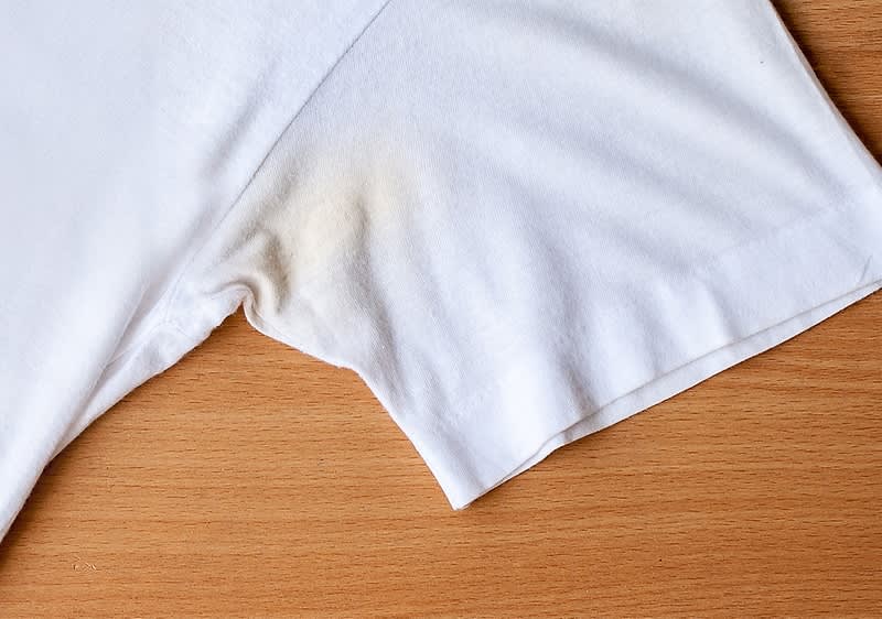 Tricou alb cu pete galbene sub braț pe masă de lemn