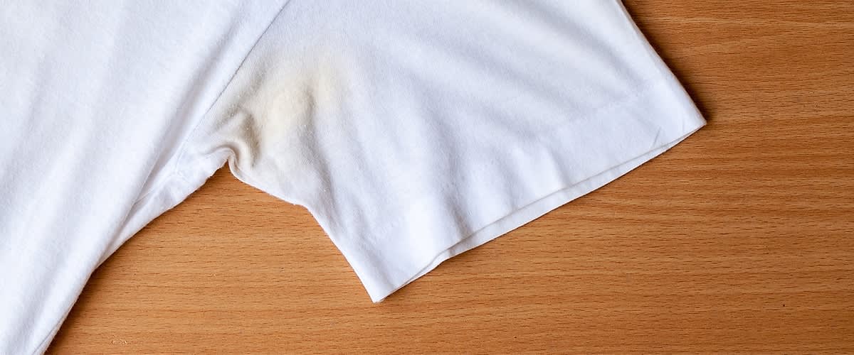 Tricou alb cu pete galbene sub braț pe masă de lemn