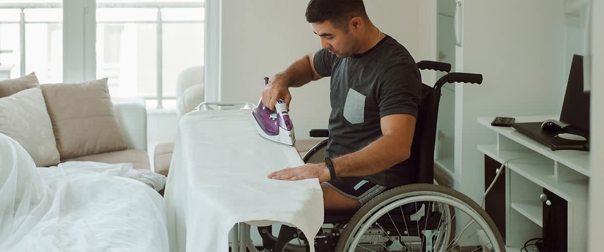 Persoană în scaun cu rotile călcând haine pe masă de călcat