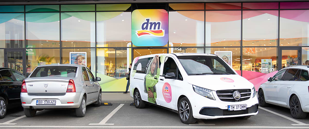 Mașină Mercedes albă parcată în fața magazinului DM