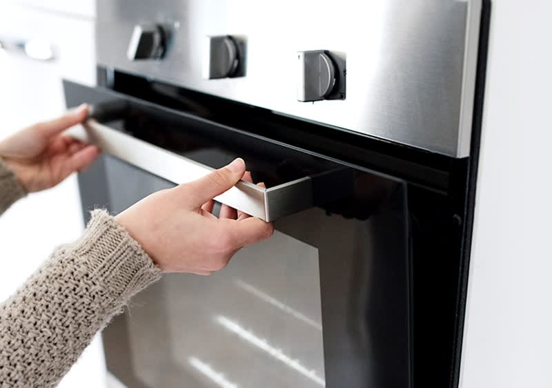 Persoană deschizând ușa unui cuptor modern din inox