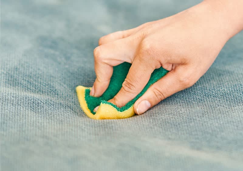 Mână curățând o suprafață cu un burete galben și verde