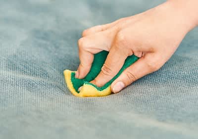Mână curățând o suprafață cu un burete galben și verde