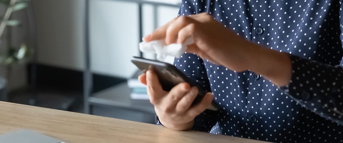 Persoană curățând ecranul unui telefon mobil cu o cârpă