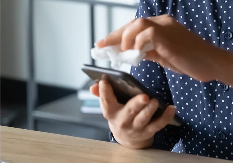 Persoană curățând ecranul unui telefon mobil cu o cârpă