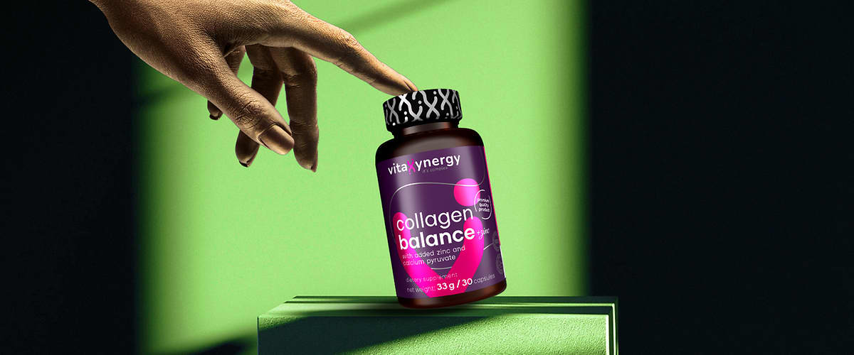 Mână atingând sticla de supliment collagen balance pe fundal verde