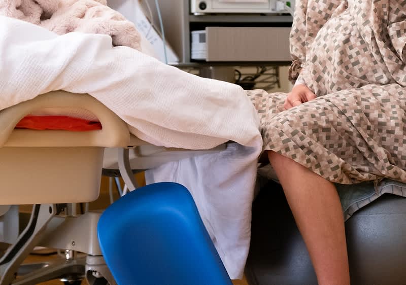 Femeie gravidă în halat stând pe minge de exerciții lângă pat de spital