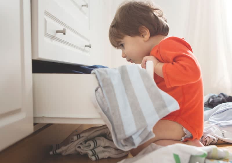 Copil în pijama roșie căutând în sertar cu haine