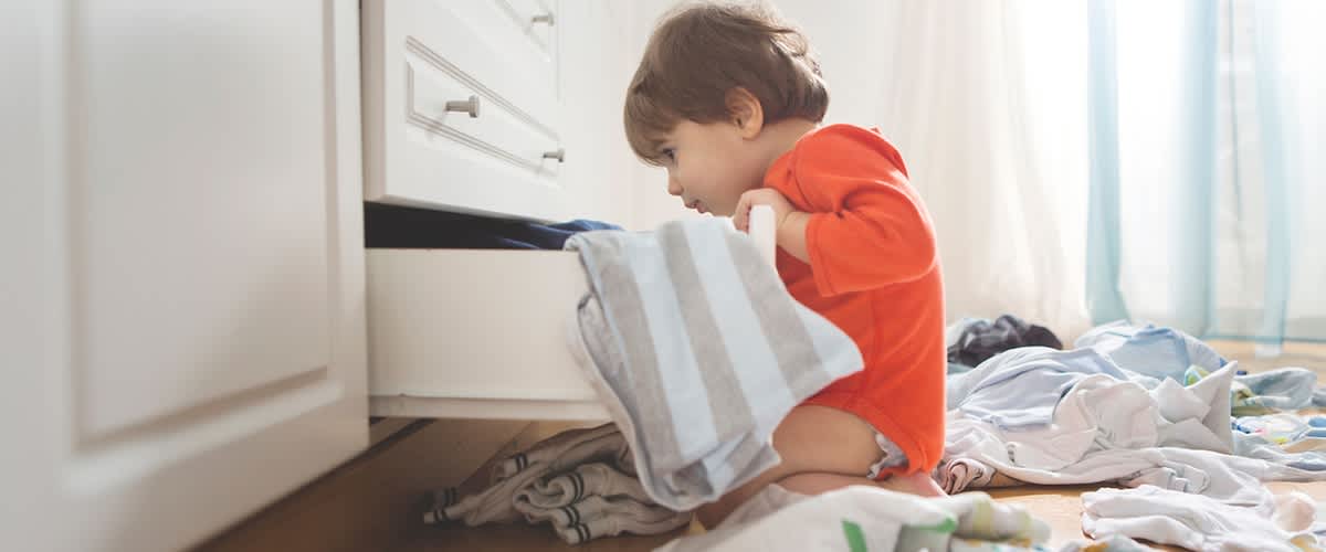 Copil în pijama roșie căutând în sertar cu haine