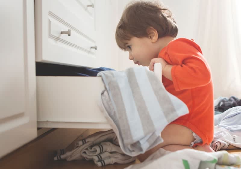 Copil în pijama roșie căutând în sertar cu haine