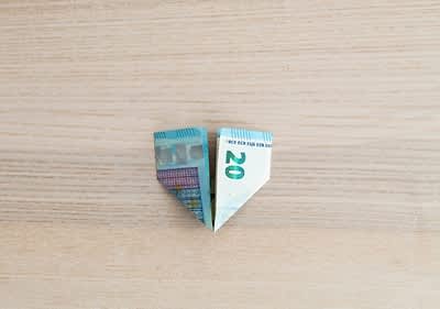Bancnotă de 20 de euro pliată în formă de inimă pe masă de lemn