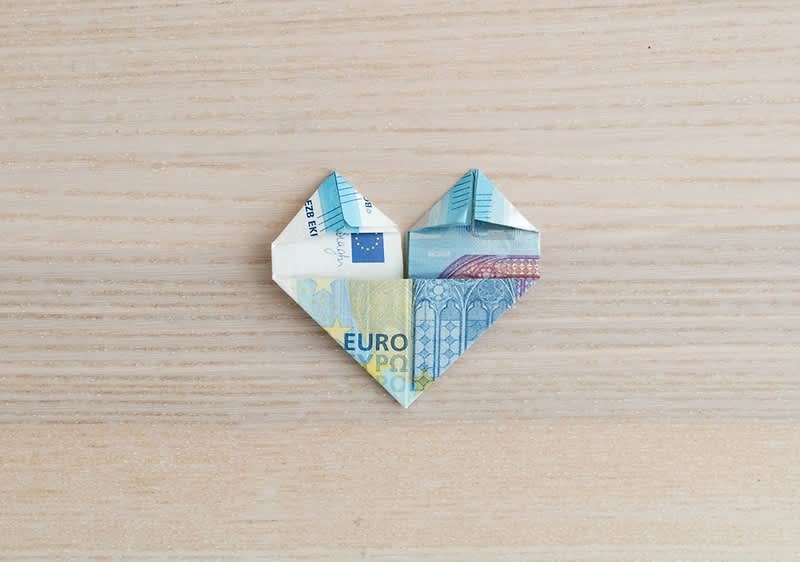 Bancnotă euro pliată în formă de inimă pe fundal de lemn