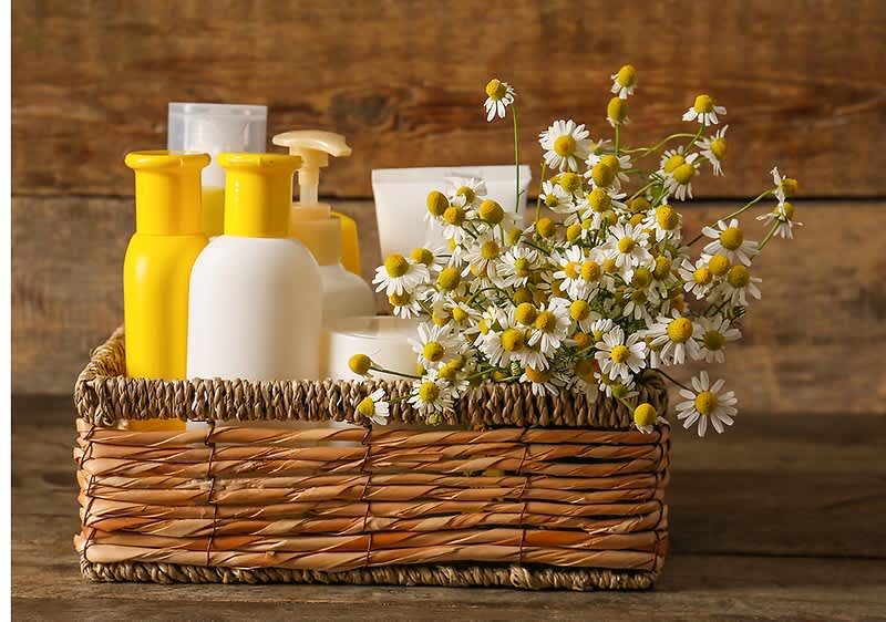 Produse cosmetice și flori de mușețel într-un coș de răchită