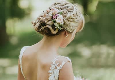 Coafură de nuntă elegantă cu flori în păr și rochie albă