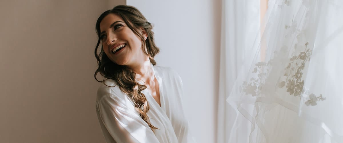 Persoană în rochie albă lângă fereastră cu perdea albă