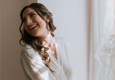 Persoană în rochie albă lângă fereastră cu perdea albă