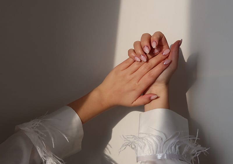 Mâini cu unghii roz pal și manșete cu pene în lumină naturală