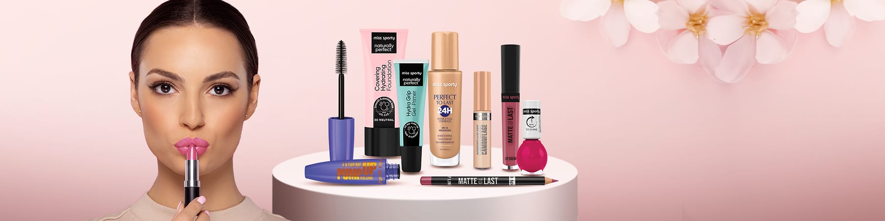 Produse cosmetice diverse pe un suport alb cu fundal roz și flori albe