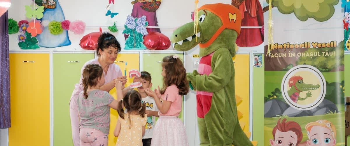 Copii interacționând cu o mascotă de crocodil într-o sală decorată