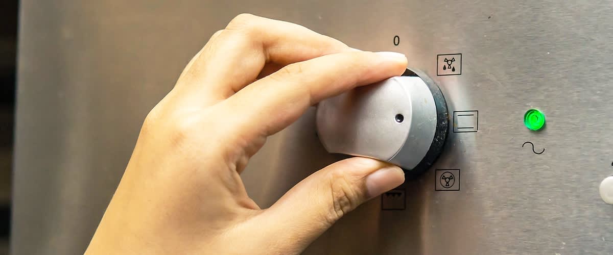 Mână ajustând un buton rotativ pe un cuptor electric