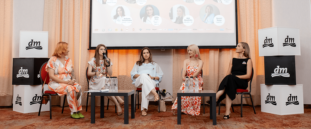 Cinci femei stând pe scaune la un panel de discuție în interior