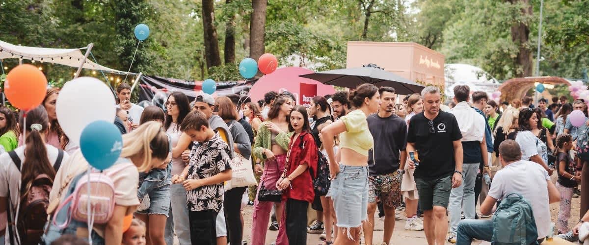 O mulțime de oameni la un festival în aer liber cu baloane și copaci