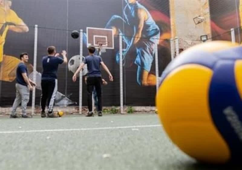 Tineri jucând baschet pe teren cu mural și minge de volei în prim-plan