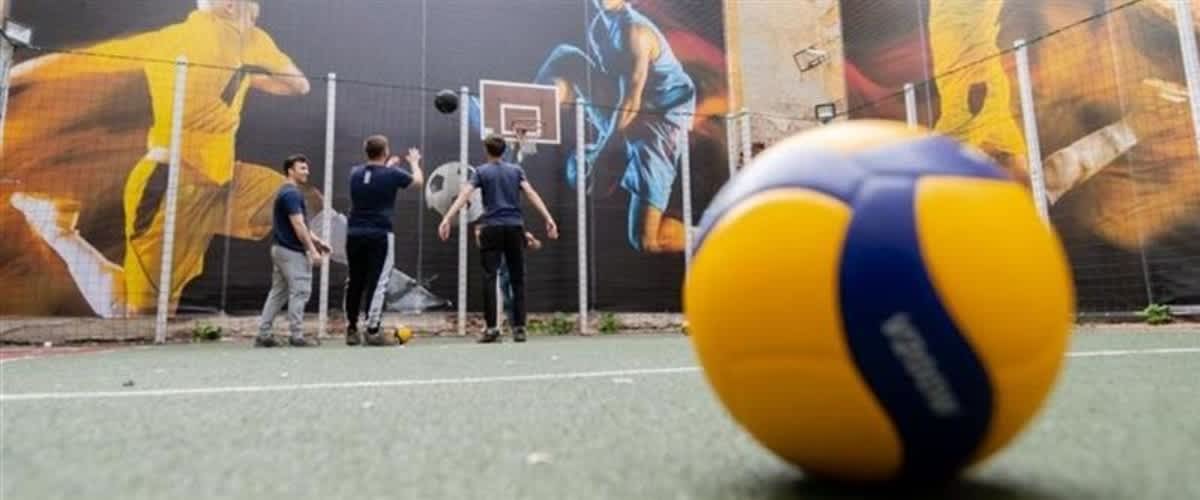 Tineri jucând baschet pe teren cu mural și minge de volei în prim-plan