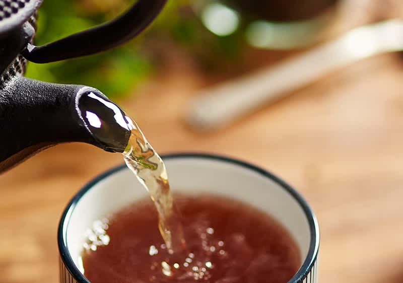 Ceainic turnând ceai într-o ceașcă pe o masă de lemn