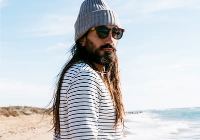 Persoană pe plajă purtând căciulă și ochelari de soare cu vedere la mare