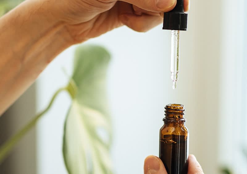 O mână ținând o pipetă deasupra unei sticle de ulei esențial