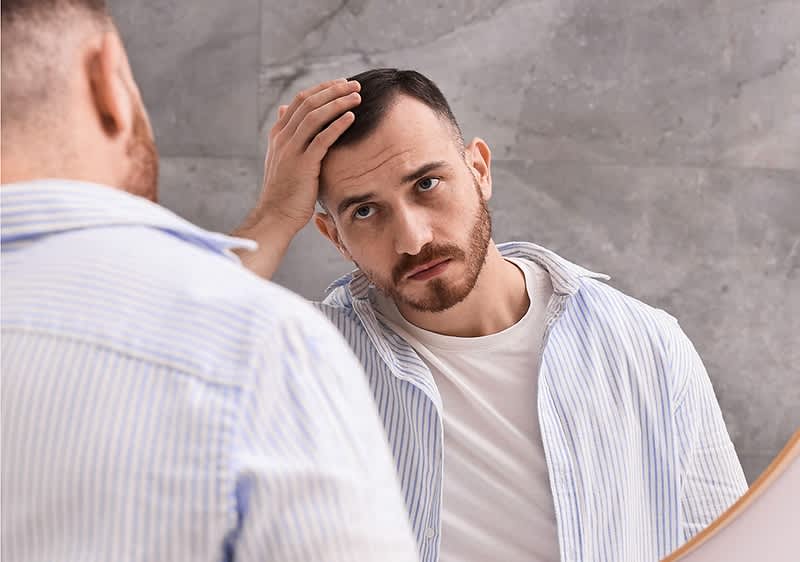 Bărbat în cămașă dungi verificându-și părul în oglindă