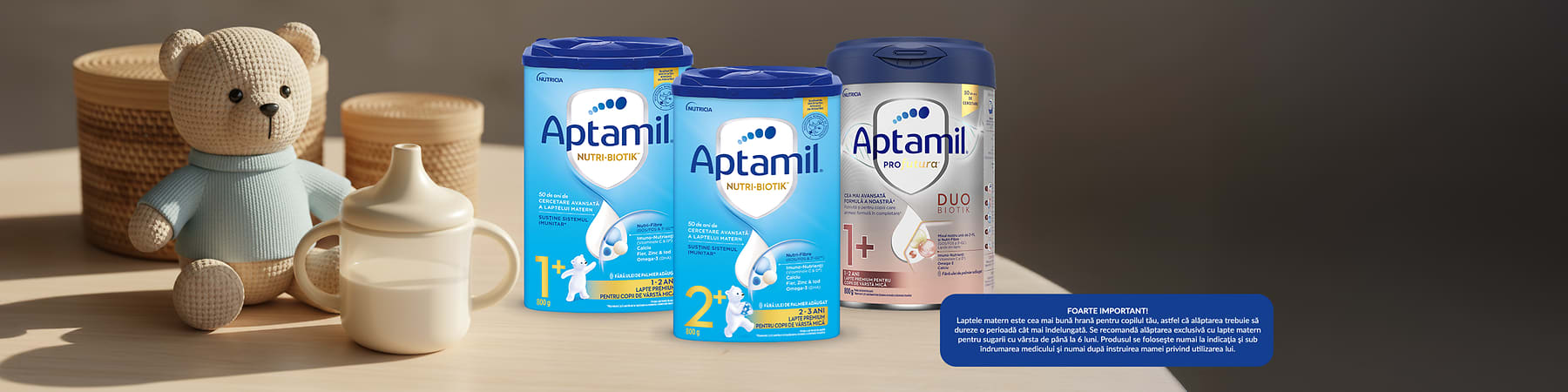 Trei cutii de lapte praf Aptamil lângă un ursuleț și o sticlă pentru bebeluși