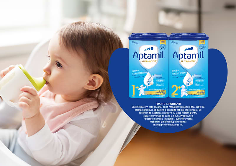 Bebeluș în scaun înalt cu cutii de lapte praf Aptamil