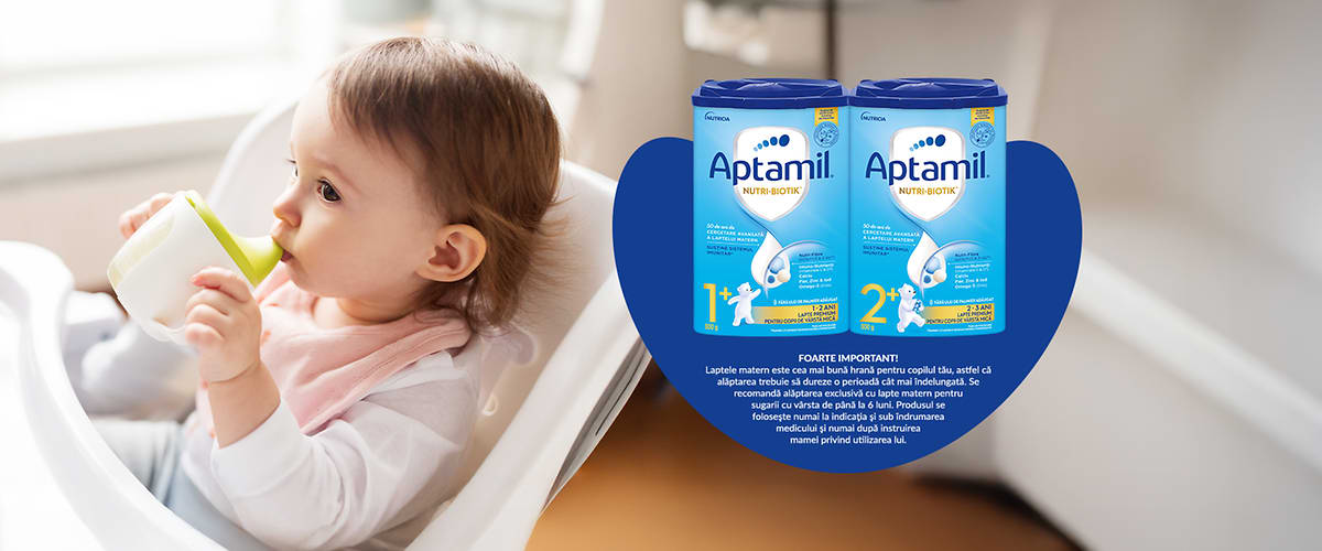 Bebeluș în scaun înalt cu cutii de lapte praf Aptamil