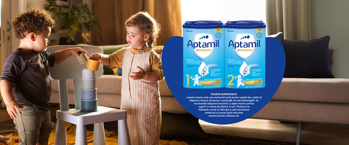 Două copii jucându-se lângă cutii de lapte praf Aptamil