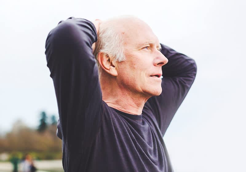 Bărbat în vârstă cu fața blurată, mâinile pe cap, fundal exterior