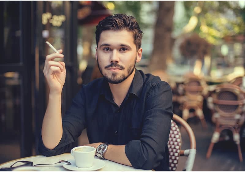 Bărbat la o cafenea ținând o țigară și o ceașcă de cafea pe masă