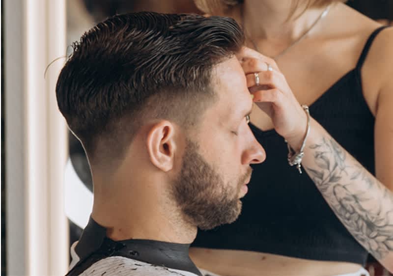 Client la frizerie cu tunsoare proaspătă și stilistă tatuată