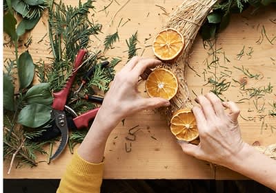 Persoană creând un decor de Crăciun cu portocale uscate și crenguțe de brad