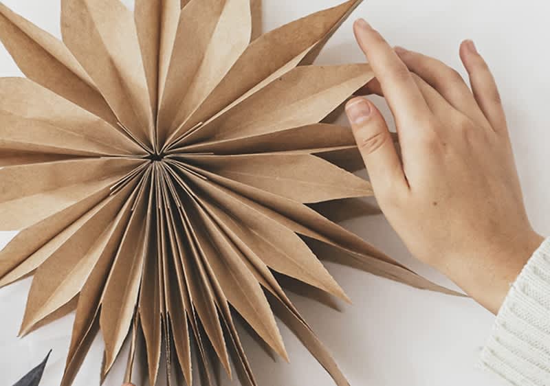 O mână atinge o stea de origami din hârtie maro